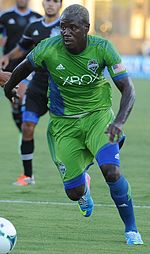 A man wearing a green soccer uniform, playing soccer.