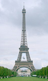 An avenue of trees leads to a large iron lattice tower, in which an oversized rugby ball hangs within the lower sections.