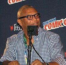 Reginald Hudlin seated at a table for a public talk