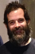 A middle-aged man with brown hair and a bushy brown beard smiling at the camera.