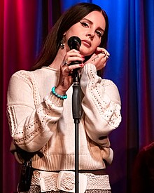 Woman holding microphone with other hand by ear with a frown.