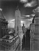 Distant aerial view of a 70-story building with several setbacks and a pyramidal roof; a flagpole sits stop the roof.