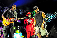 Three men on stage, one of whom is holding a guitar.