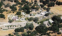 A view from above of a large property in a semi-desert. The landscape is pale with clumps of vegetation. The property shows circular structures between the buildings.