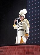 Swift singing onto a mic, dressed as a drum majorette