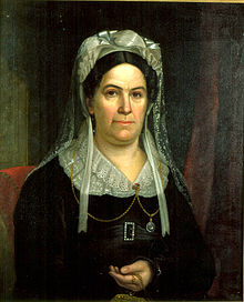 Woman in black with white bonnet and lace collar looking forward