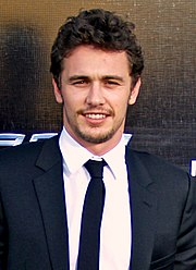 An image of a dark-haired male smiling while wearing a navy jacket over a white-collared shirt.