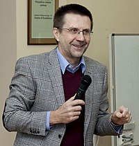 A smiling, bespectacled man speaking into a microphone