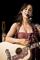 A woman holding a guitar in front of a microphone.