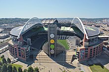 An open-air stadium with two arched roofs and a center tower that rises from a stairway and plaza