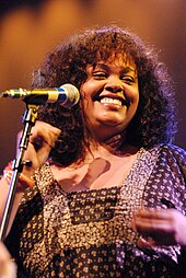 A woman wearing a brown dress while smiling and snapping her fingers.