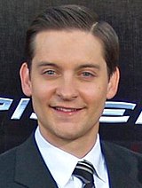 An image of a Caucasian man smiling. He has medium brown hair and is wearing a navy jacket over a white shirt and striped tie.