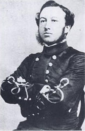 photograph of a man sitting upright, wearing a grey dress uniform