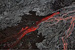 Aerial photograph of volcanic rock, with black cold lava split by a bright river of red lava