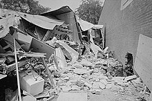 A black and white photograph of a building in ruins next to an intact wall