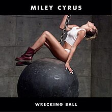 An image of Miley Cyrus sitting on a wrecking ball while holding on to a chain that is attached to it.