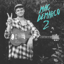 Picture of Mac DeMarco and his guitar. He is smiling and wearing a baseball cap.