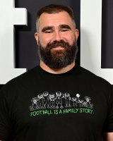 Jason Kelce Smiles Directly at Camera wearing Black T-Shirt that Reads "Football Is A Family Story." in green font