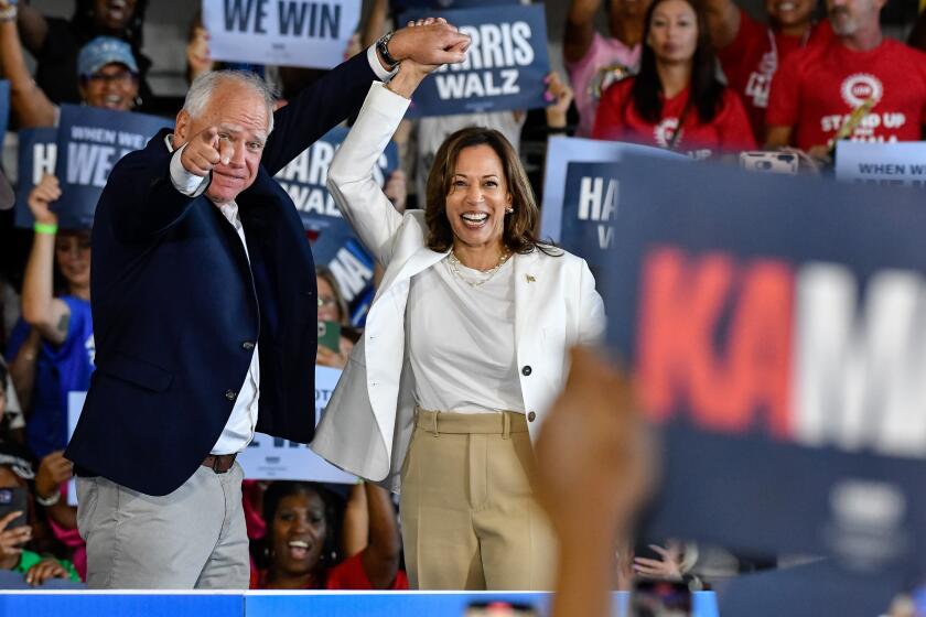 ROMULUS, MICHIGAN - AUGUST 7: Vice Presidential nominee Tim Walz raises the hand of Presidential nominee Kamala Harris as she takes the stage to speak to several thousand attendees at her presidential campaign rally at Detroit Metropolitan Wayne County Airport in Romulus, MI on August 7, 2024. (Photo by Adam J. Dewey/Anadolu via Getty Images)