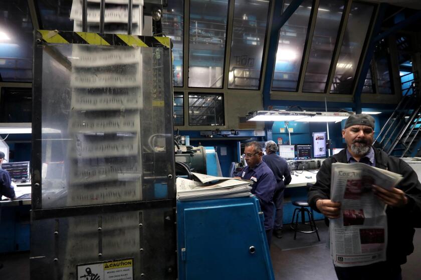 LOS ANGELES, CA - FEBRUARY 15, 2024 - - A pressman looks over a paper for possible print corrections as a conveyor belt transports newspapers from the press room, pictured, to the first floor where the newspapers are packaged and distributed at the Los Angeles Times Olympic Printing Plant in Los Angeles on February 15, 2024. Press operators review the run of newspapers with color on all but one of the 22 pages. They start at 8:30 p.m. and print a little more than 100,000 copies and finish in less than two hours. The last edition of the LA Times will roll of the presses on March 10. (Genaro Molina/Los Angeles Times)