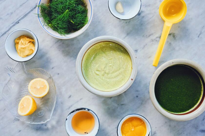 An overhead photo of aioli components on white marble: bowls of dill oil, vinegar, a bunch of fresh dill and a citrus juicer