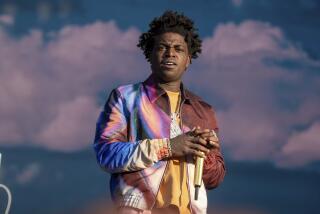 Kodak Black scowls while wearing a colorful bomber jack and holding a golden microphone 