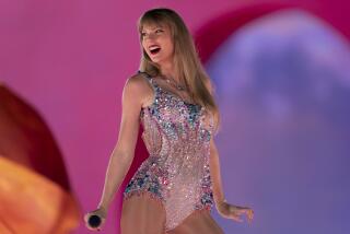 Taylor Swift in a bejeweled body suit standing on a stage with a mic in hand and looking to her right