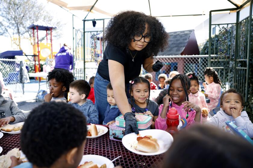 An adult puts a paper plate of food on a table with seated children around it.