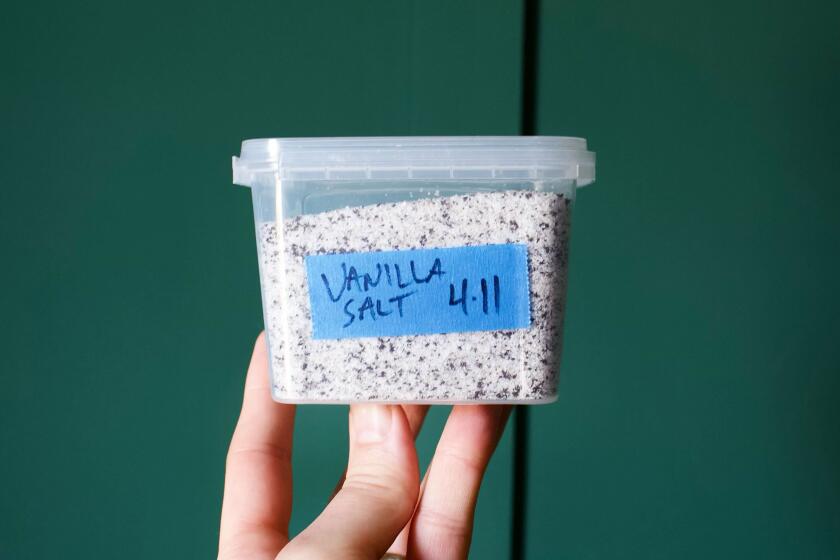 A hand holds a plastic container of vanilla-flecked salt against green wall at Santa Monica restaurant Bar Monette