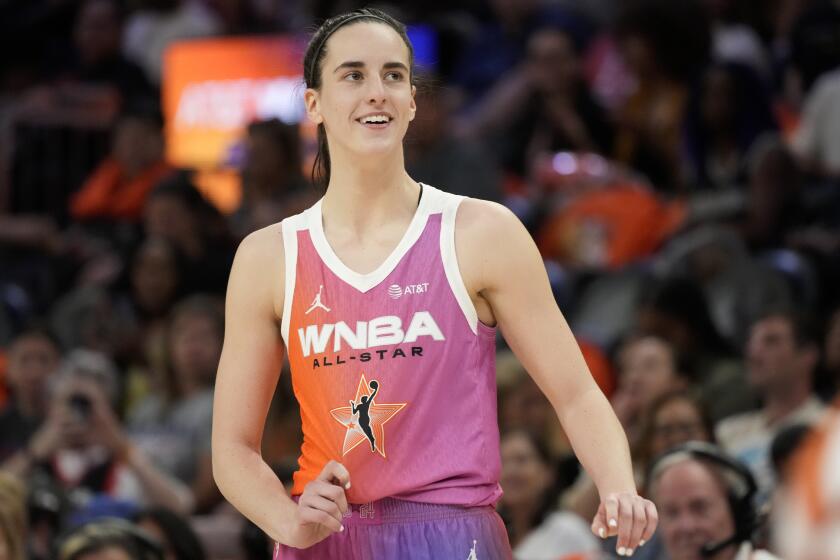 Caitlin Clark smiles and tugs on her All-Star jersey as she pauses on the court during the WNBA All-Star basketball game