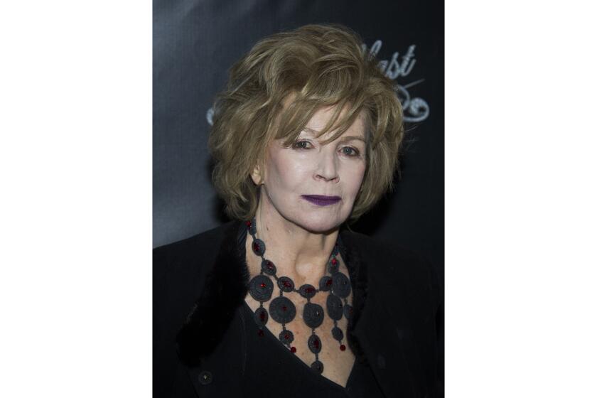 An older woman with a voluminous short hairdo wearing a large black necklace and a dark dress