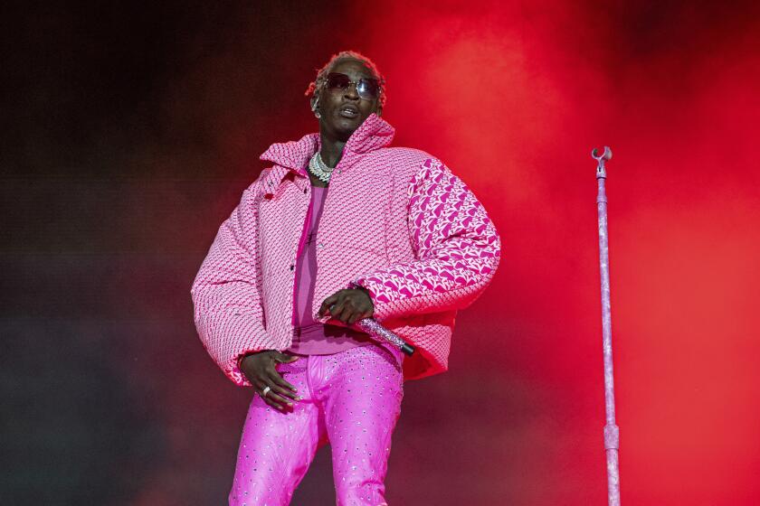 A performer onstage wearing sunglasse, a puffy pink jacket and tight pink pants