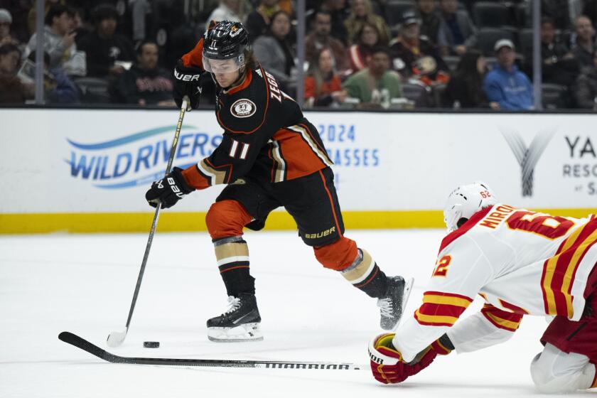 Ducks forward Trevor Zegras, left, controls the puck in front of Calgary Flames defenseman Daniil Miromanov.