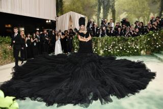 Cardi B wears a large black turban and a voluminous black down on a green carpet