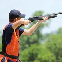 Young man skeet shooting with airborne shell