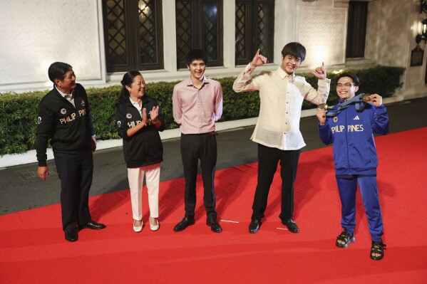 Olympic double gold medalist in gymnastics, Carlos Yulo, right, poses with President Ferdinand Marcos Jr., left, First Lady Liza Araneta Marcos, second from left, and their sons during a welcome ceremony at the Malcañang presidential palace in Manila, Philippines on Tuesday, Aug. 13, 2024. (AP Photo/Basilio Sepe, Pool)