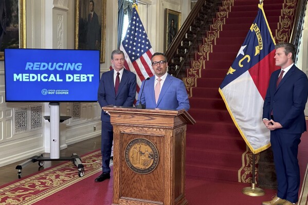 Undue Medical Debt board member Jose N. Penabad, center, speaks, while Gov. Roy Cooper, left, and state Health and Human Services Secretary Kody Kinsley listen on Monday, Aug. 12, 2024, at the Executive Mansion in Raleigh, N.C. (AP Photo/Gary D. Robertson)