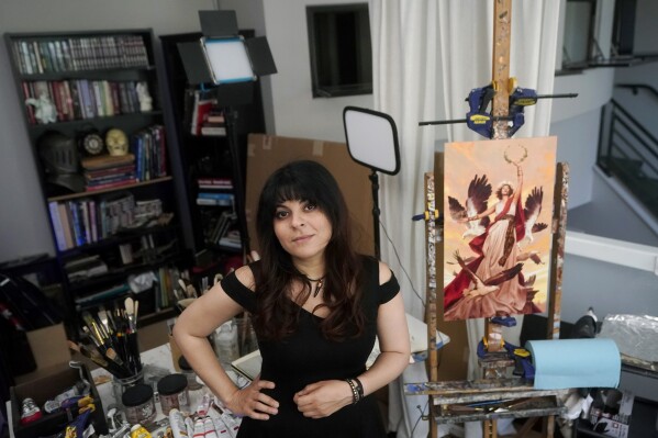 FILE - Artist Karla Ortiz poses next to one of her paintings, right, in San Francisco, Aug. 4, 2023. The version of the painting uploaded online belies a hidden defense system — a tool called Glaze that masks the artist's style and cloaks the art from use by generative AI. (AP Photo/Jeff Chiu, File)