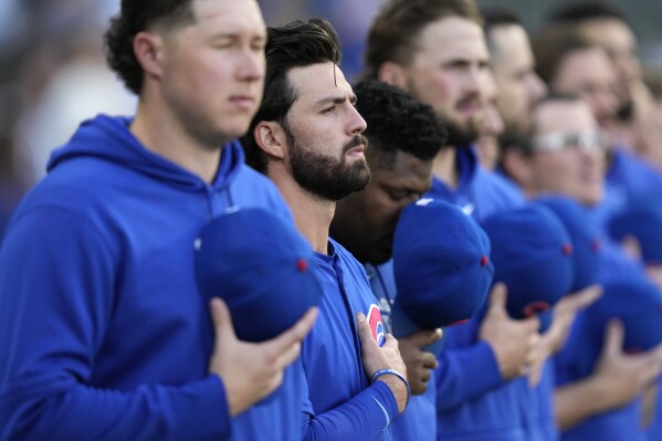 Chicago Cubs shortstop Dansby Swanson, second from left, stands with his hand over his heart during the national anthem before a baseball game against the Chicago White Sox on Saturday, August 10, 2024, in Chicago. The Cubs' shortstop went from a bundle of nerves to unbridled joy as he watched alone on a couch in his basement. His wife Mallory scored the lone goal in a 1-0 win over Brazil to propel the Americans to their fifth gold medal. (AP Photo/Charles Rex Arbogast)