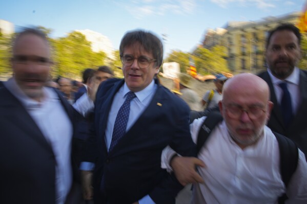 Accompanied by his lawyer Gonzalo Boye, second right, Catalan independence leader and former President Carles Puigdemont, second from left, arrives to allegedly attend the investiture debate in Barcelona, Spain, Thursday, Aug. 8, 2024. The search for former Catalan president and pro-independence leader Carles Puigdemont by the Mossos d'Esquadra has clogged the main roads, resulting in traffic jams. The officers have activated operation 'cage' to locate the former president, who remains missing after returning to Barcelona following seven years of avoiding arrest for organizing an independence referendum in 2017. (AP Photo/Emilio Morenatti)