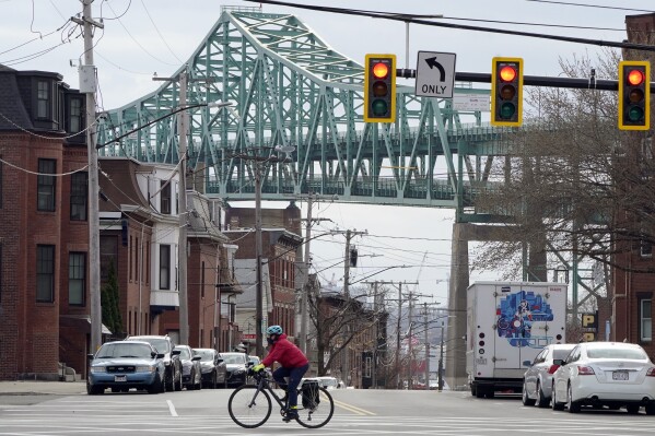 FILE - A cyclist rides along a street near the Tobin Memorial Bridge, background, in Chelsea, Mass., on Wednesday, March 31, 2021. After nearly 1,750 low-income people in the Boston suburb won a lottery to receive monthly stipends from the city from November 2020 to August 2021, researchers found that winners visited emergency departments significantly less than people who did not receive the monthly payments. (AP Photo/Steven Senne, File)