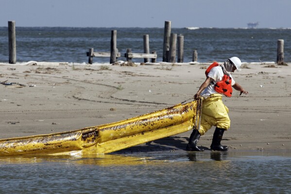 FILE - A worker pulls an oil boom that a current pinned against a pier in Caminada Pass in Grand Isle, La., May 22, 2010. When a deadly explosion destroyed BP's Deepwater Horizon drilling rig in the Gulf of Mexico, tens of thousands of ordinary people were hired to help clean up the environmental devastation. These workers were exposed to crude oil and the chemical dispersant Corexit while picking up tar balls along the shoreline, laying booms from fishing boats to soak up slicks and rescuing oil-covered birds. (AP Photo/Patrick Semansky, File)