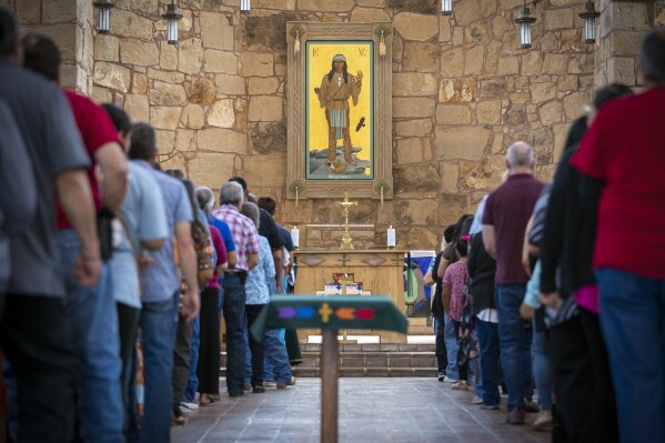 Mescalero Apache Tribe members and parishioners wait in line to receive Communion during a Mass at the St. Joseph Apache Mission church in Mescalero, New Mexico, Sunday, July 14, 2024. Behind the altar is the Apache Christ painting, an icon that depicts Christ as a Mescalero medicine man. (AP Photo/Andres Leighton)