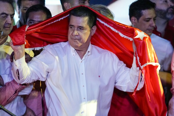 FILE - Former President Horacio Cartes covers himself with a flag of the ruling, Colorado party after the polls closed during the general election in Asuncion, Paraguay, April 30, 2023. The Biden administration on Tuesday, Aug. 6, 2024, slapped sanctions on a Paraguayan tobacco company for financing Cartes, a cigarette tycoon whom the White House sanctioned in 2023 for corruption. (AP Photo/Jorge Saenz, File)