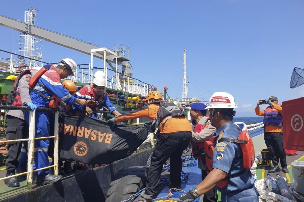 In these handout photo, released by Indonesia Police, Indonesian police and rescue team members carry a body bag containing the body of a victim of the fire on the Elisabeth tanker in the Gili Tepekong area of the Karangasem district, Bali, Indonesia, Wednesday, Aug. 7, 2024. (AP Photo/Handout Indonesia Police)