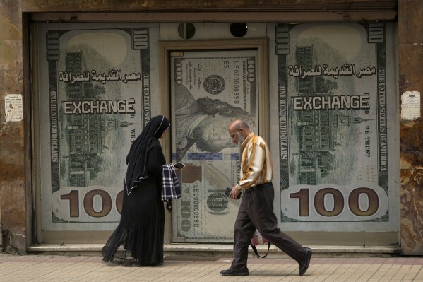 FILE - Egyptians walk past an exchange office in Cairo, Egypt, Wednesday, March 6, 2024. The Egyptian pound is sliding against foreign currencies, inching closer to EGP 50 to the U.S. dollar on Monday, Aug. 5, after a recent hike in subway fares and fuel prices. (AP Photo/Amr Nabil, File)