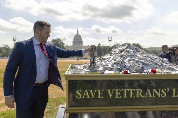 In this photo provided by the Heroic Hearts Project, Jesse Gould adds 22 dog tags signifying the number of veterans estimated to die by suicide in one day, at a memorial paying tribute to the estimated 150,000 veterans who have lost their lives to suicide over the past 20 years, displayed near the U.S. Capitol in Washington on July 10, 2024. (Michael Schoen/Heroic Hearts Project via AP)