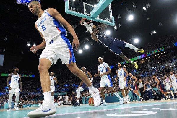 United States' LeBron James, right dunks as France's Nicolas Batum walks away during a men's gold medal basketball game at Bercy Arena at the 2024 Summer Olympics, Saturday, Aug. 10, 2024, in Paris, France. (AP Photo/Mark J. Terrill)