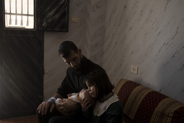 Palestinian boxer Muazzaz Abayat, 37, holds his 2-month-old son Mohammed and daughter Mira, 5, at home in the West Bank city of Bethlehem, Wednesday, July 17, 2024, days after his release from Israeli prison, frail, disoriented and with no initial memory of his family. (AP Photo/Maya Alleruzzo)