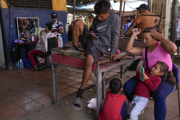 Carla Machado, right, waits with her children for her husband who cuts hair at a flea market in Maracaibo, Venezuela, Monday, July 22, 2024. The country's presidential election is set for July 28. (AP Photo/Matias Delacroix)